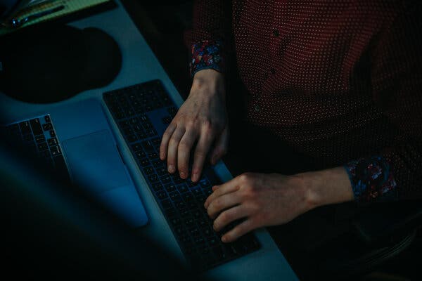 A pair of hands at a keyboard in a darkened room.